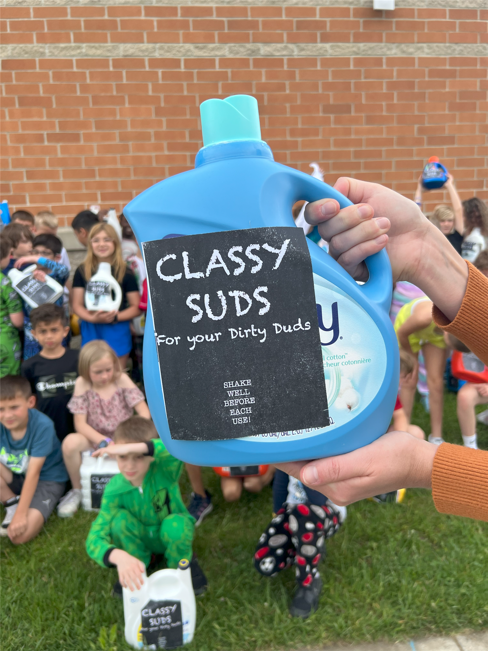  JUGS OF "CLASSY SUDS" BEING HELD UP IN FRONT OF GROUP OF STUDENTS